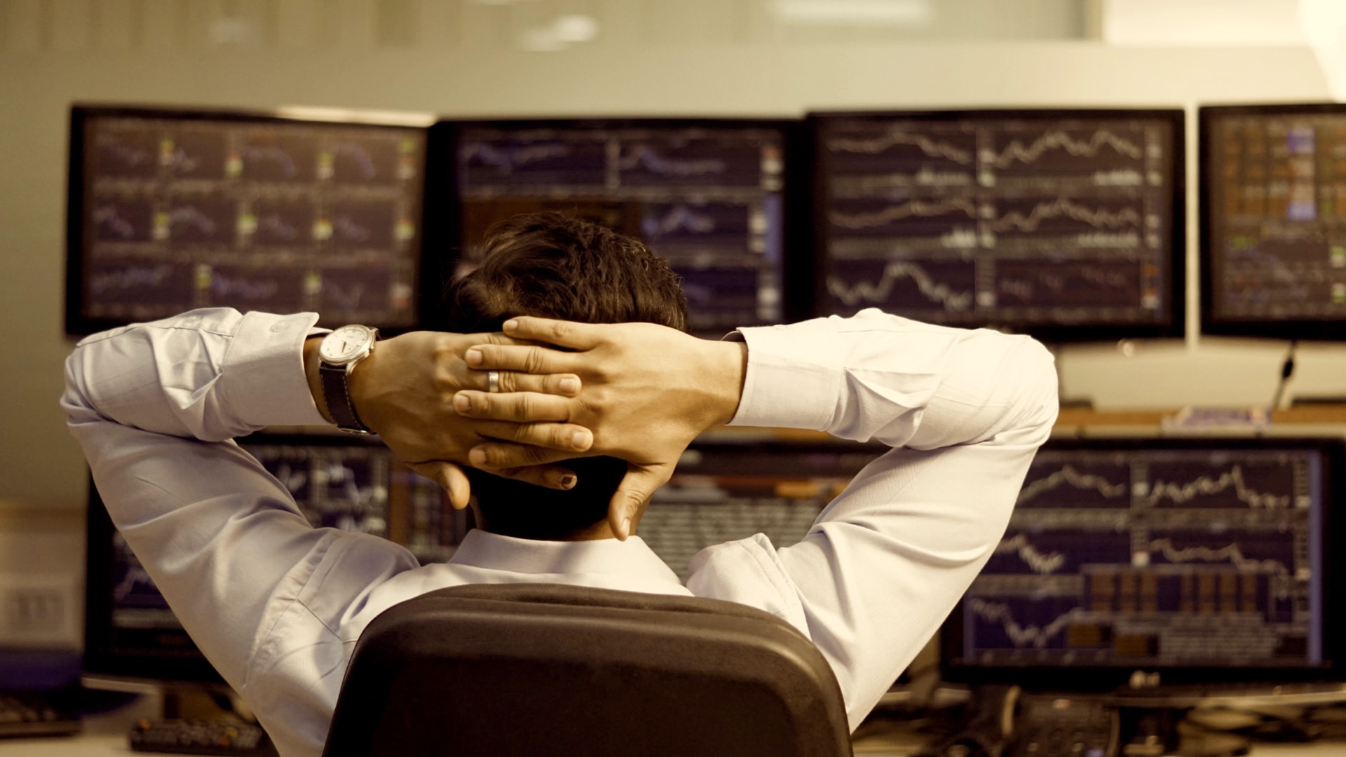 A trader studying financial markets across a multi-screen trading desk